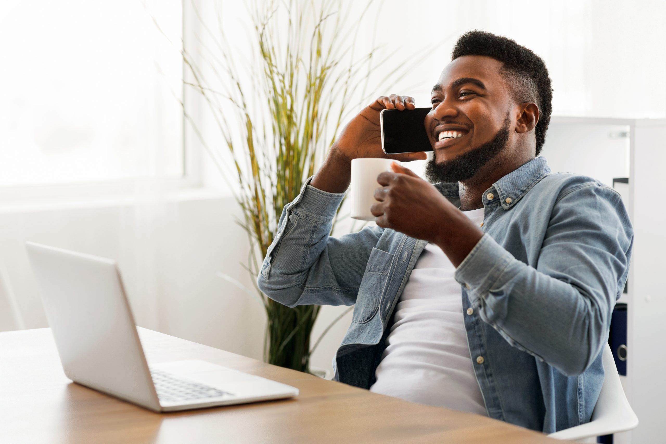 Black businessman having coffee break and taking on phone in office
