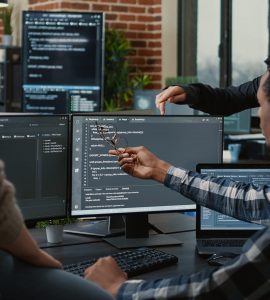 Software developers discussing about source code compiling discovers errors and asks the rest of the team for explanations in front of multiple screens running algorithms. Programmers doing teamwork.