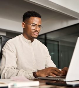 Busy serious professional African business man company employee, young male worker businessman typing on computer technology using laptop working at office, elearning at workplace desk.