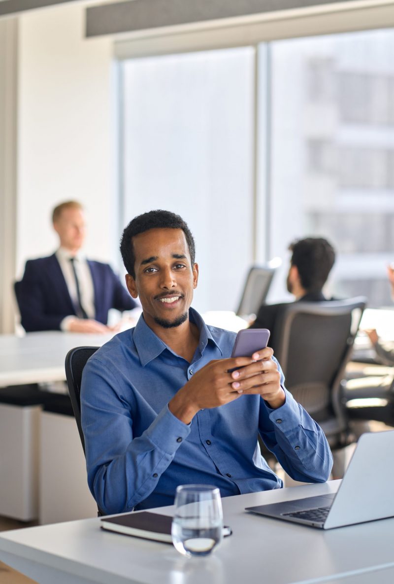 Happy young African American business man using cell phone in office. Portrait Happy young African American business man manager employee investor using cell phone in office. Male professional worker working in financial market digital mobile app on smartphone, vertical portrait