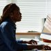Side view of young African American employee by workplace Side view of young African American employee sitting in front of computer screen by workplace and analyzing online data